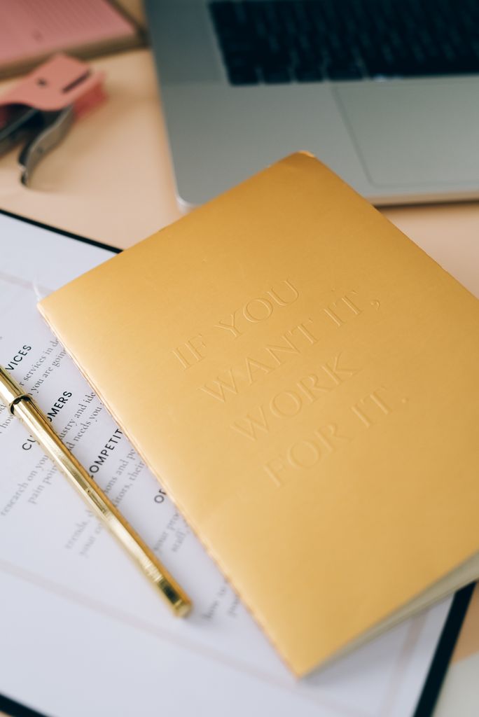A stylish office desk with a motivational notebook, laptop, and stationery, promoting productivity.