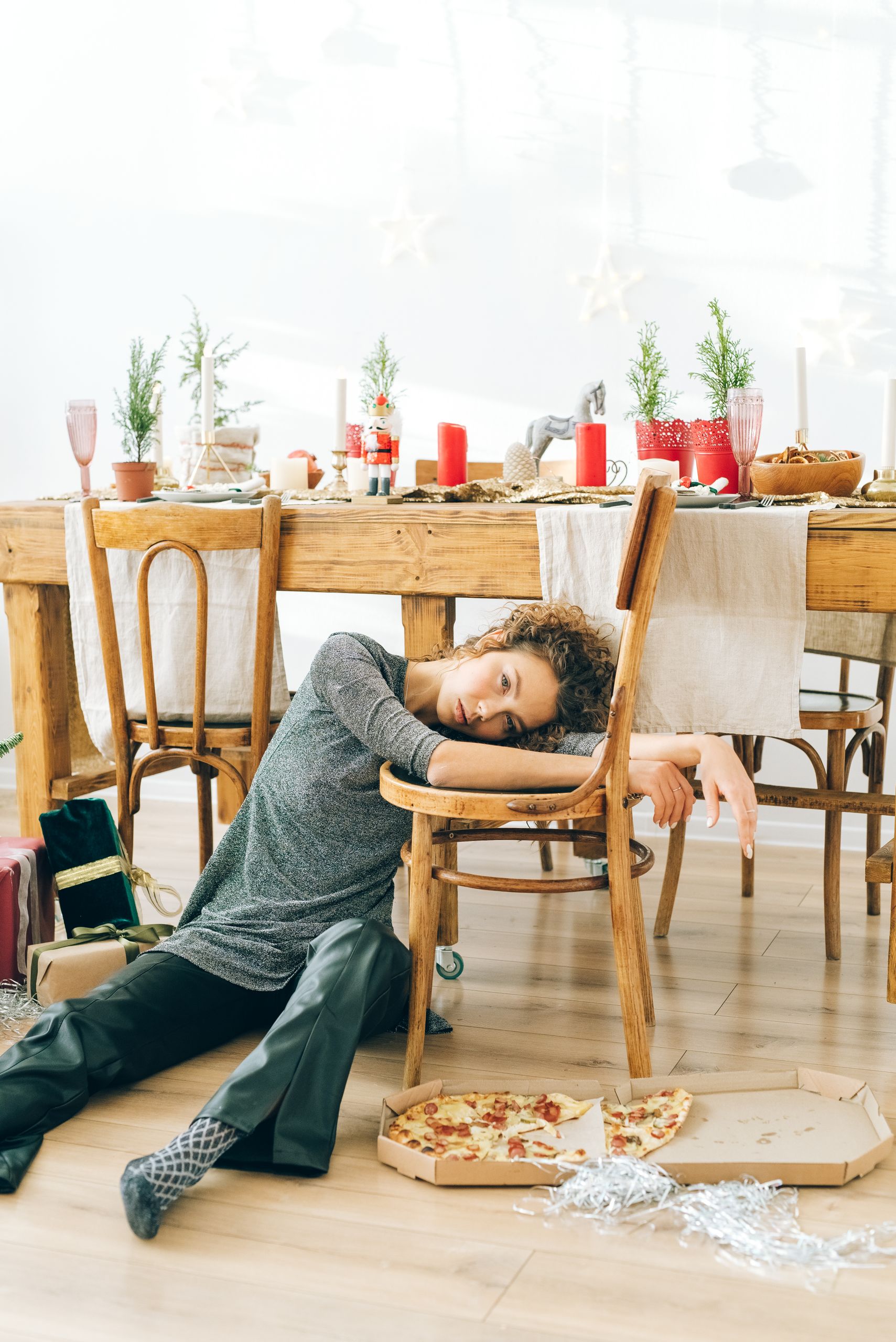 A tired woman leans on a chair next to a festive table with pizza and decorations.