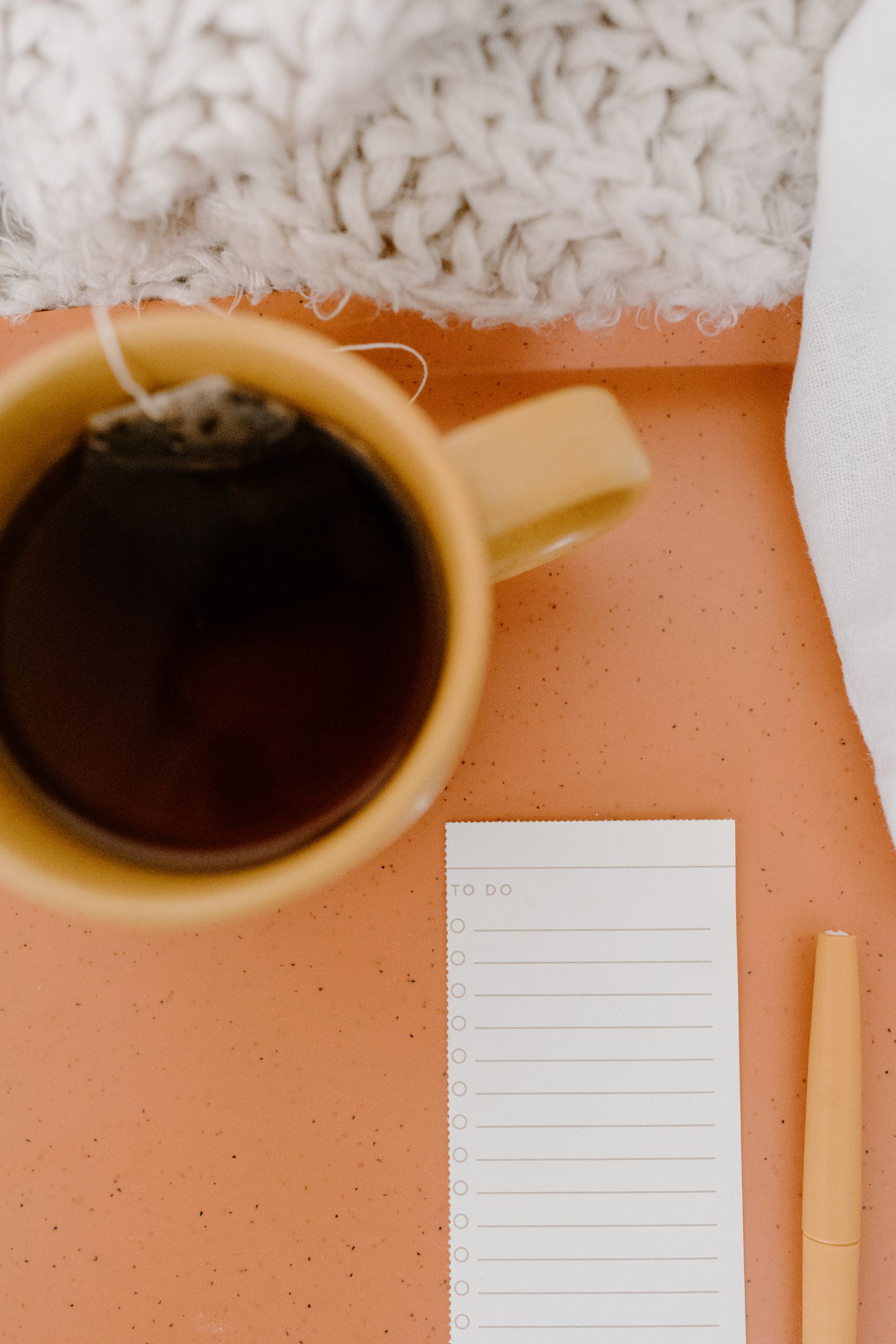 A warm and cozy flat lay featuring a cup of tea, a to-do list, and a soft blanket.
