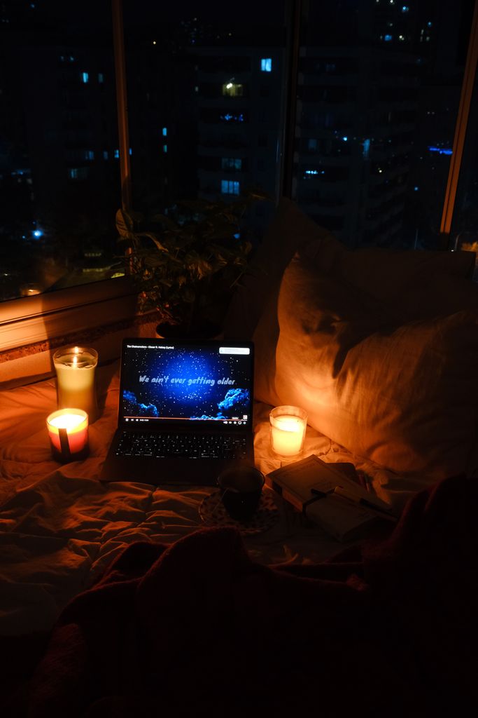 A warm nighttime setting with candles and a laptop on a bed, perfect for relaxation.