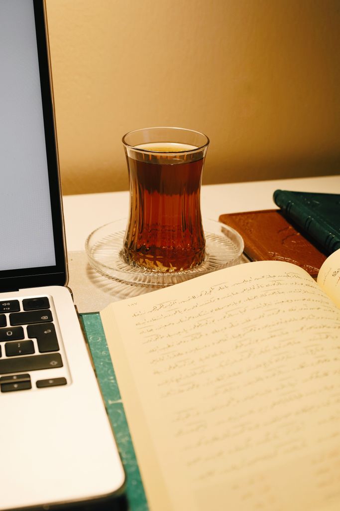 A warm workspace setup featuring tea, a notebook, and a laptop. Ideal for writing and relaxation.