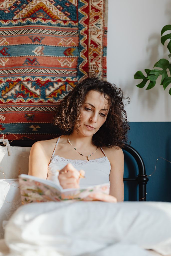 A woman enjoying leisure time writing in her journal in a cozy bedroom setting.