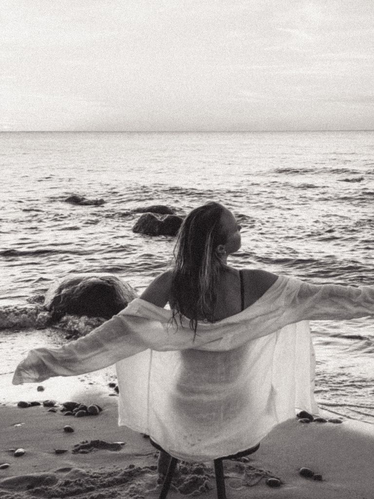A woman enjoys a peaceful moment on a sandy beach as waves gently crash ashore.