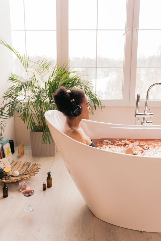 A woman enjoys a relaxing bath with headphones in a well-lit bathroom.