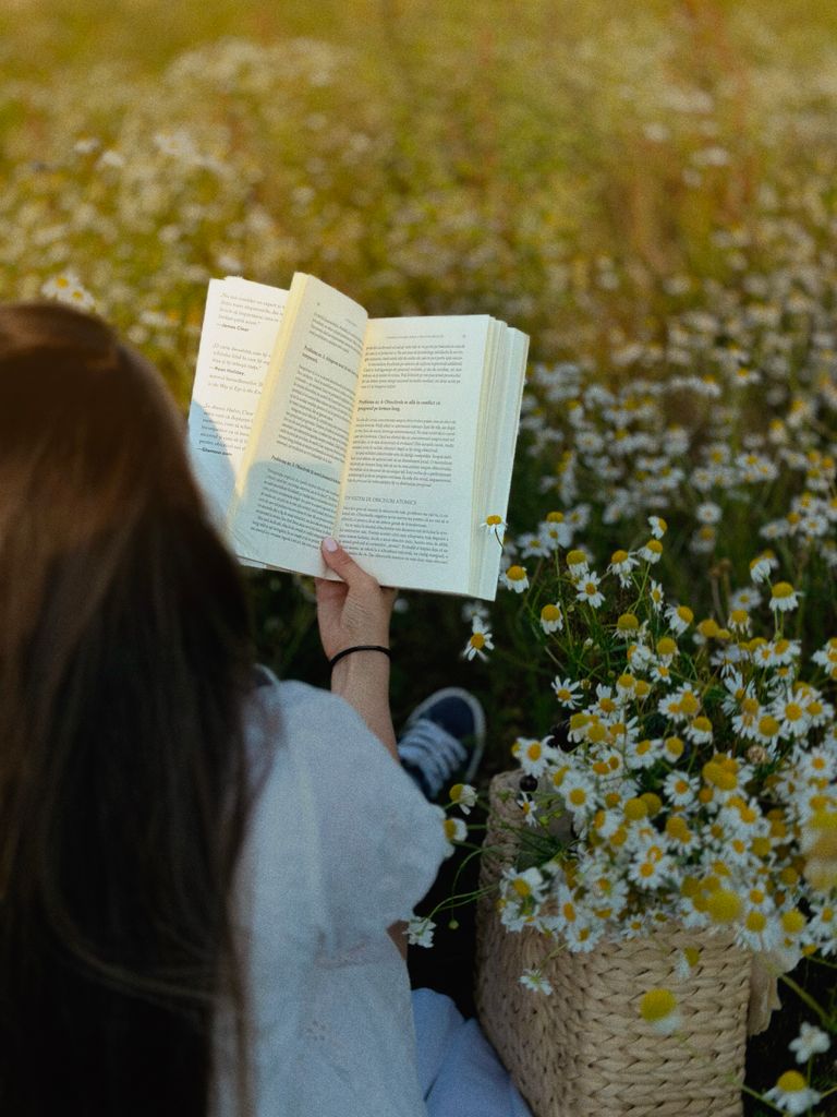 A woman enjoys reading a book in a peaceful chamomile field.