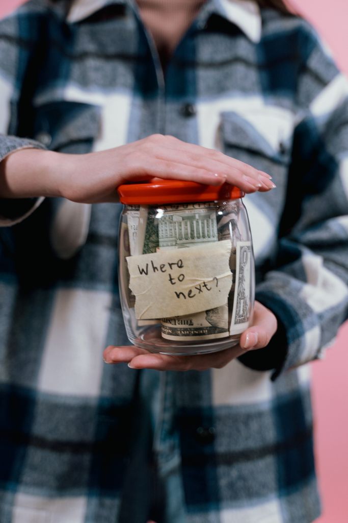 A woman holds a jar filled with money labeled 'Where to next?' symbolizing future travel plans.