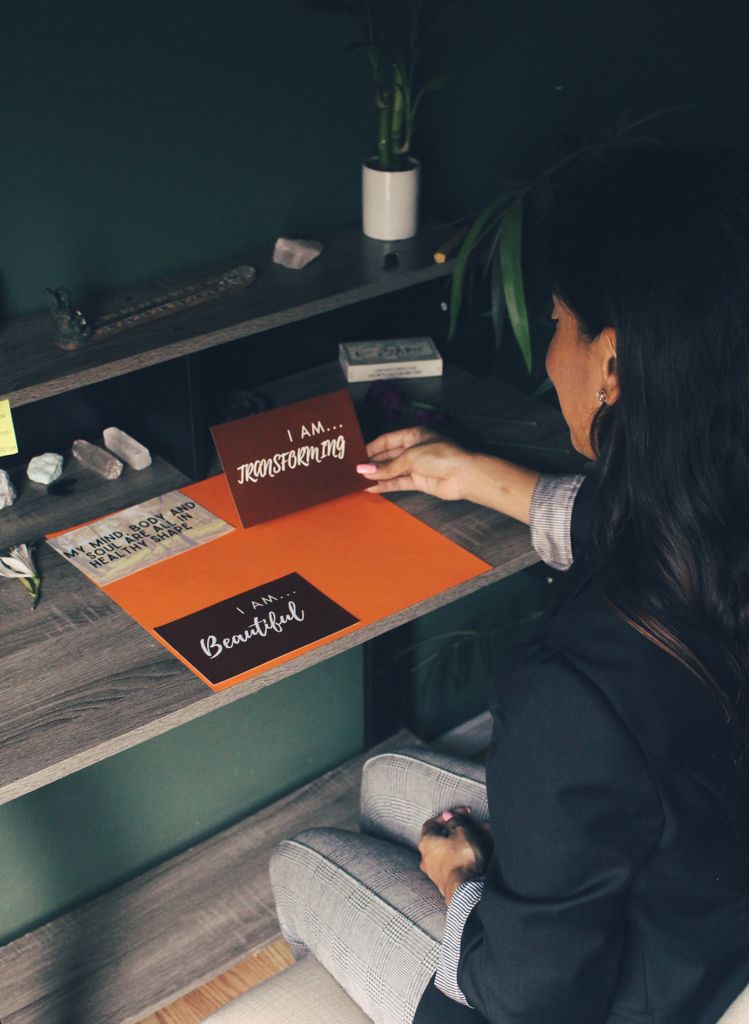 A woman reads inspirational cards at a desk, promoting self-love and motivation.