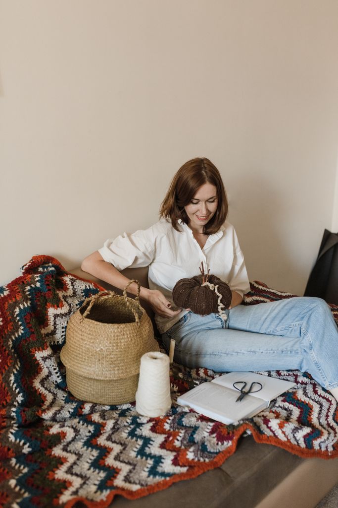 A woman sitting indoors knitting with yarn and a wicker basket, adding a cozy touch.