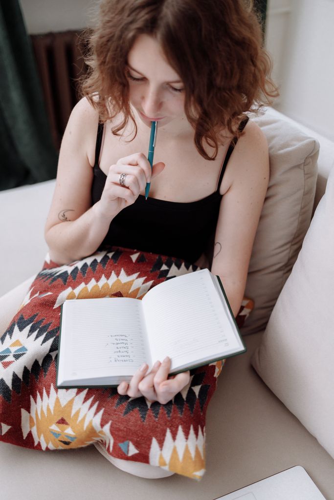 A woman sitting on a sofa, pondering while holding an open notebook and pen.winter arc checklist