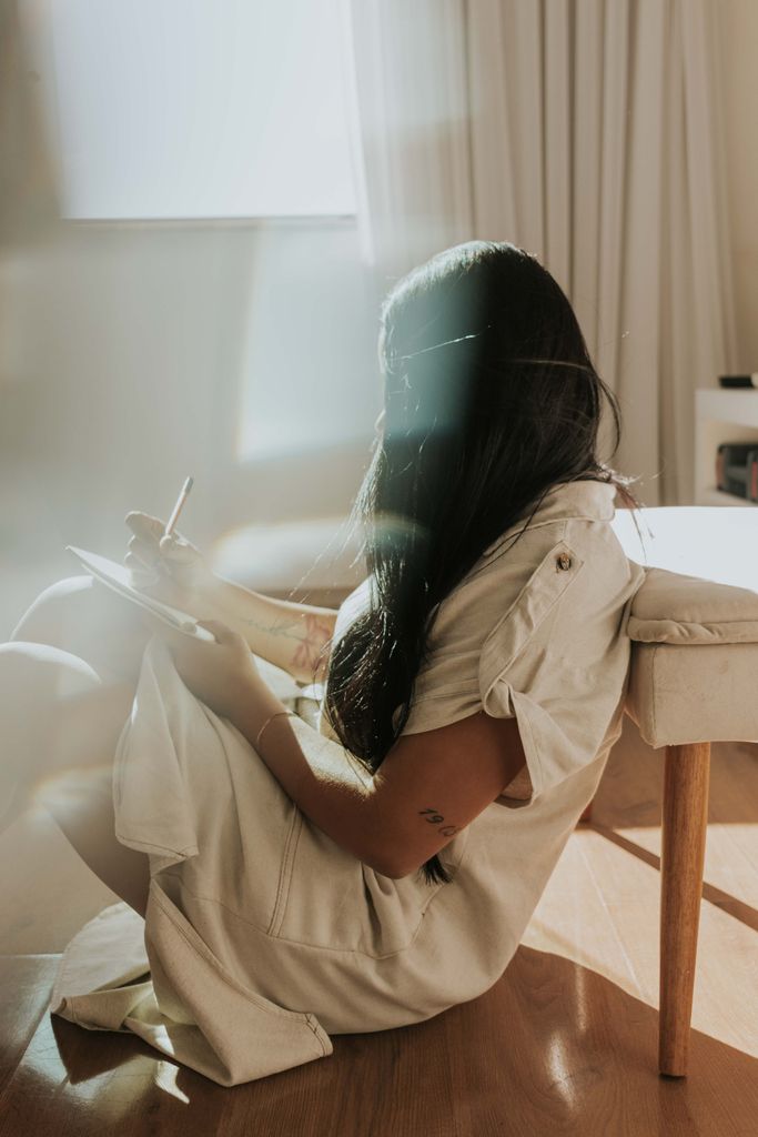 A woman sitting on the floor writing in a sunlit room, creating a serene atmosphere.