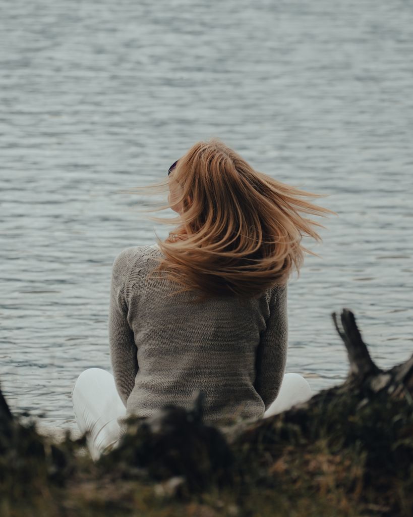A woman with flowing blonde hair sits by the sea, enjoying a moment of solitude and relaxation.