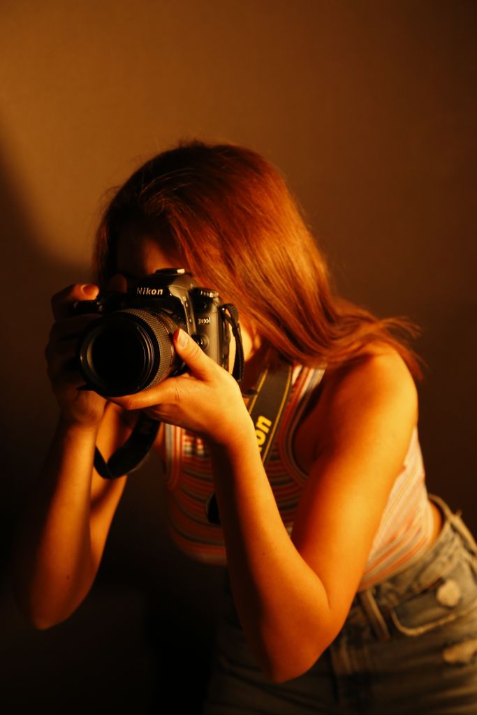 A young female photographer focuses her camera lens indoors, immersed in her craft. solo hobbies