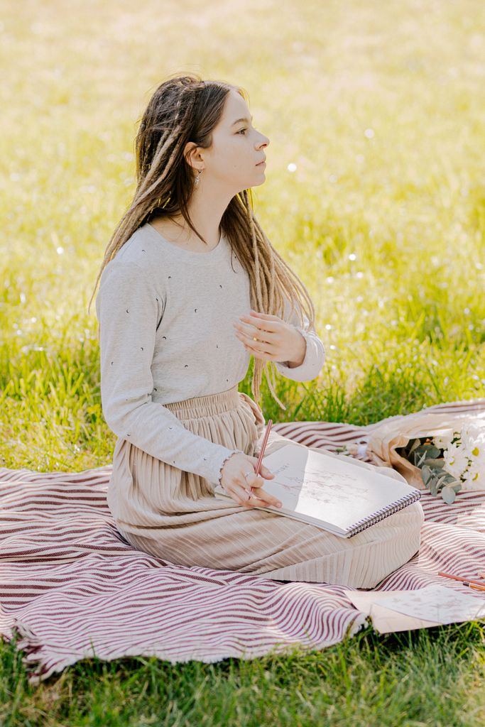 A young woman artist sketching in a park with a serene expression and relaxed posture.