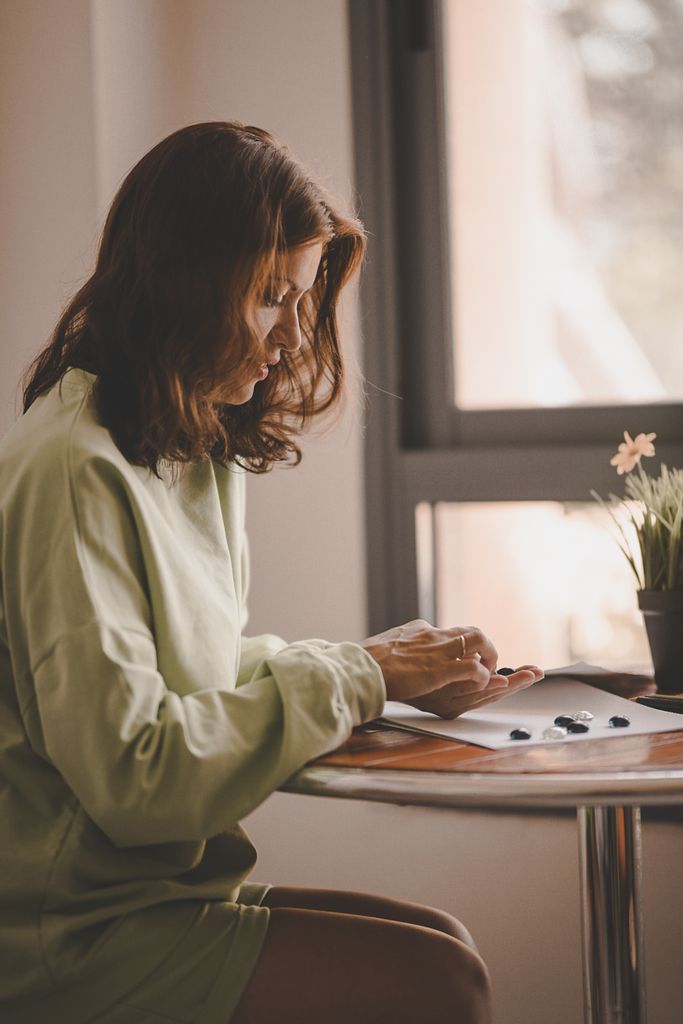 Adult woman sketching on paper at a small table near a window, in soft sunlight.