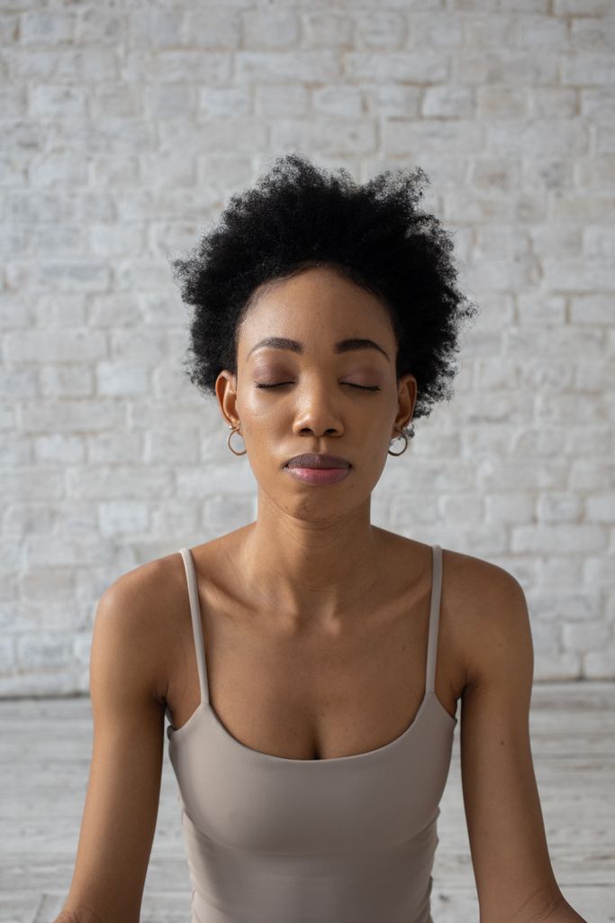 African American woman meditating with eyes closed, practicing mindfulness indoors.winter reset