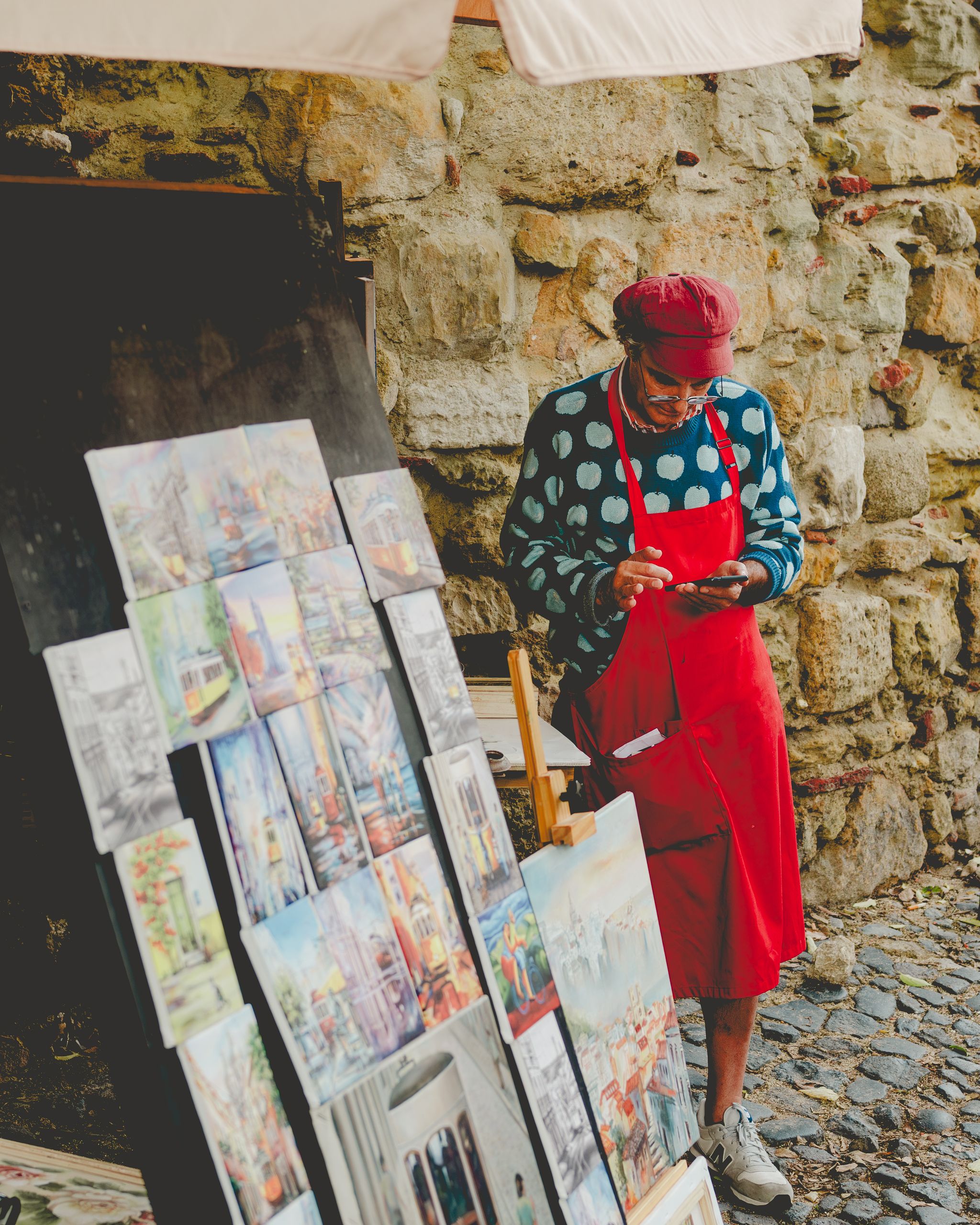 Artist in a red apron organizing paintings in an outdoor market setting.