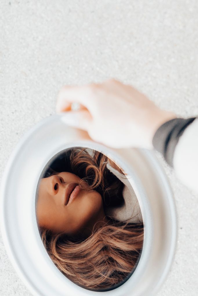 Artistic image of a woman reflected in a handheld mirror, showcasing selective focus and soft tones.
