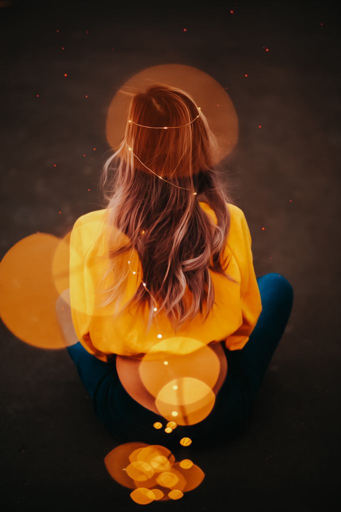 Back view of a woman sitting with fairy lights and bokeh effect, creating a dreamy atmosphere.