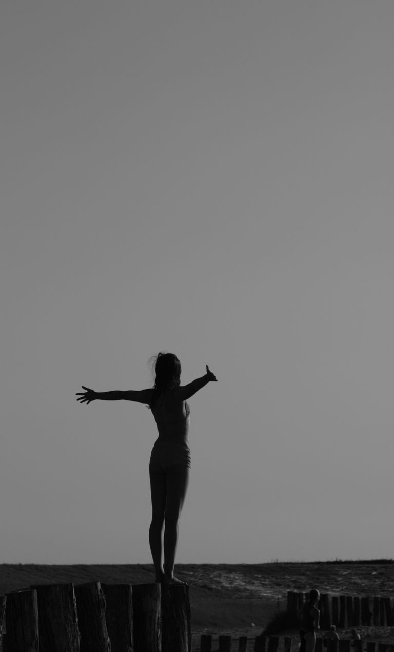 Black and white silhouette of a woman standing with open arms on a fence, symbolizing freedom.