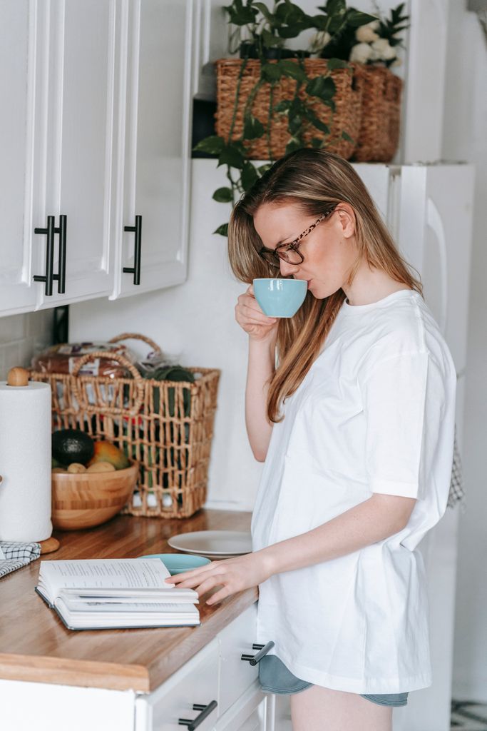 Casual woman enjoying a peaceful moment with coffee and a book in a modern kitchen setting.