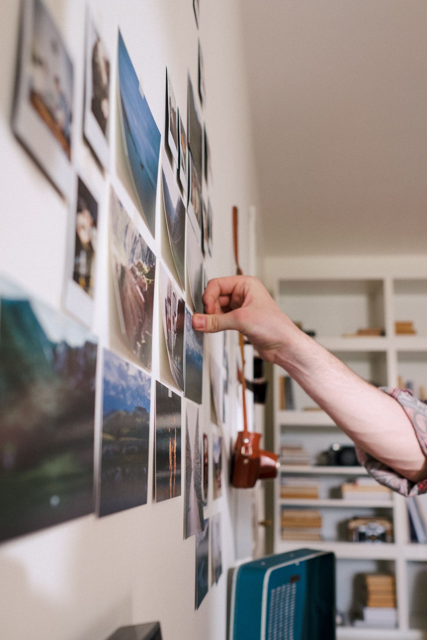 Close-up of a hand pinning photographs on a wall creating a personal photo display at home.