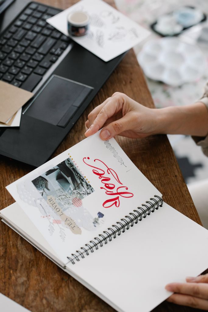 Close-up of a person holding an inspirational notebook next to a laptop on a wooden desk.