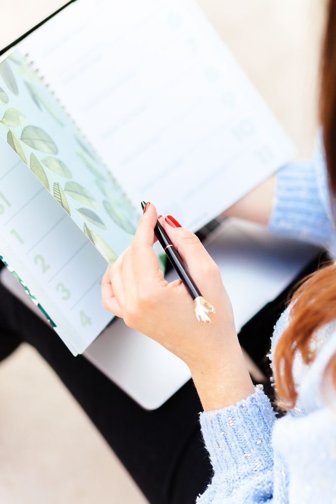 Close-up of a woman writing in a planner with a botanical design, showcasing organization and planning.