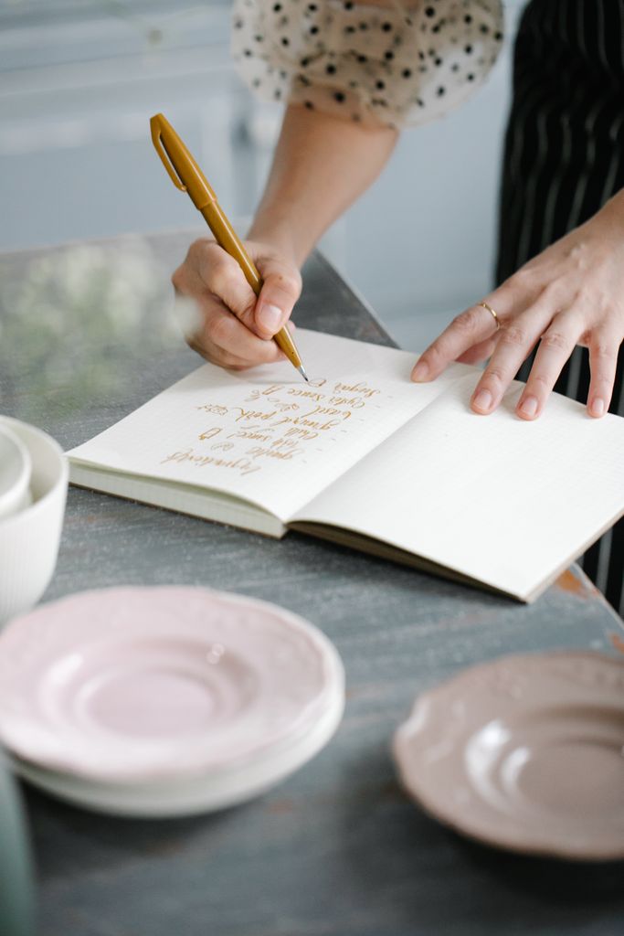 Close-up of hands writing in a notebook on a table with pink plates.