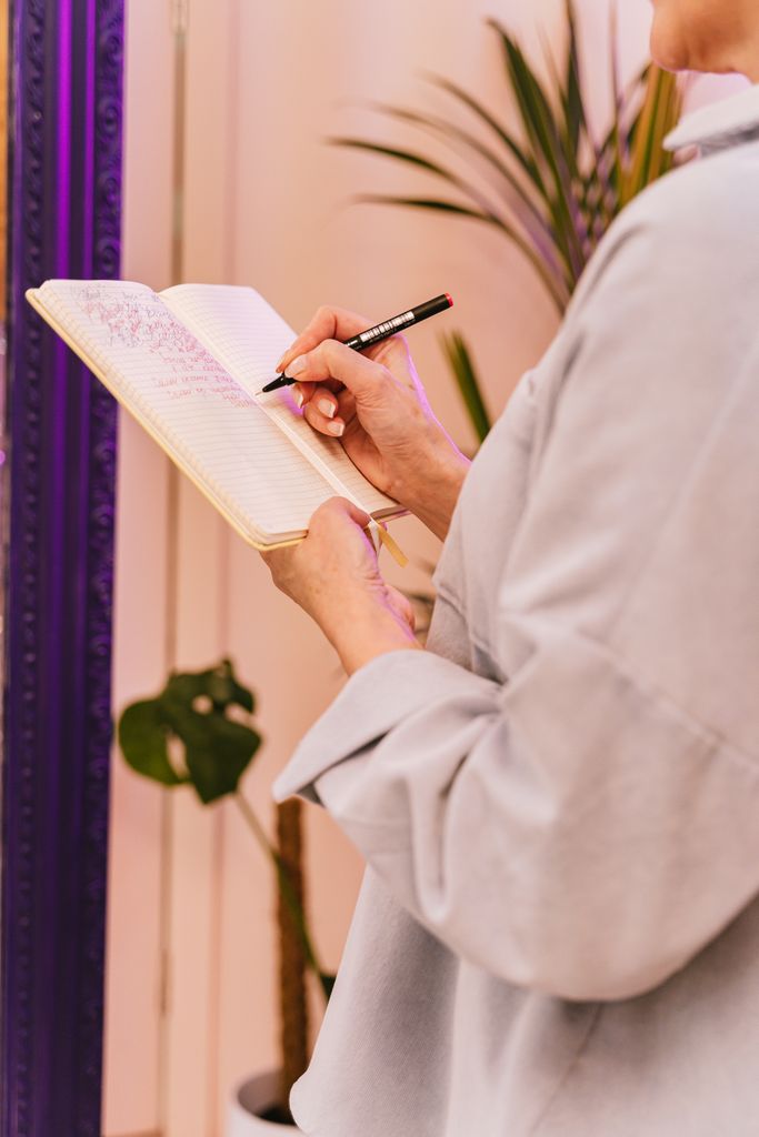 Close-up of person writing in a notebook indoors with a plant in the background.dopamine menu journal