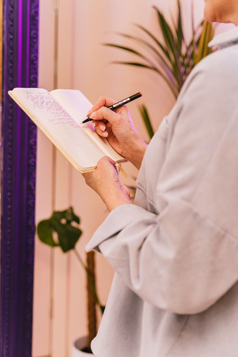 Close-up of person writing in a notebook indoors with a plant in the background.