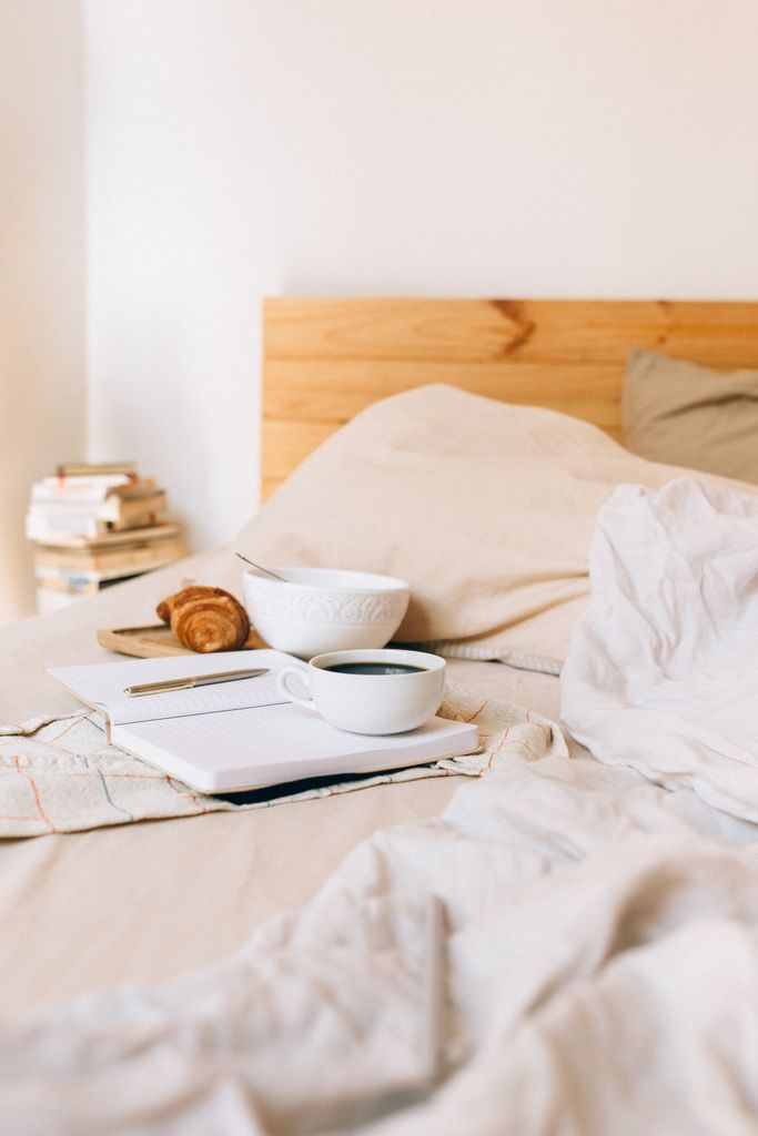 Comforting breakfast setup with coffee, pastry, and a notebook in a cozy bed environment.