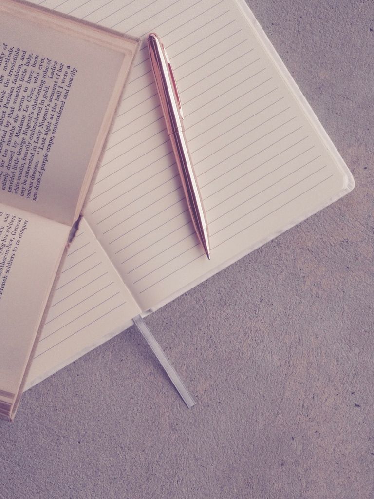Creative flatlay featuring an open book, notebook, and pen on a textured surface.