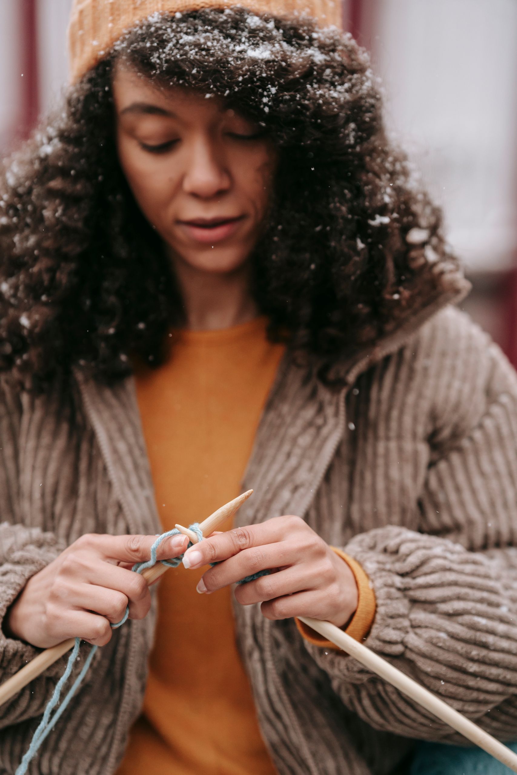 Crop focused African American female with curly hair in stylish outfit knitting on street in snowy day