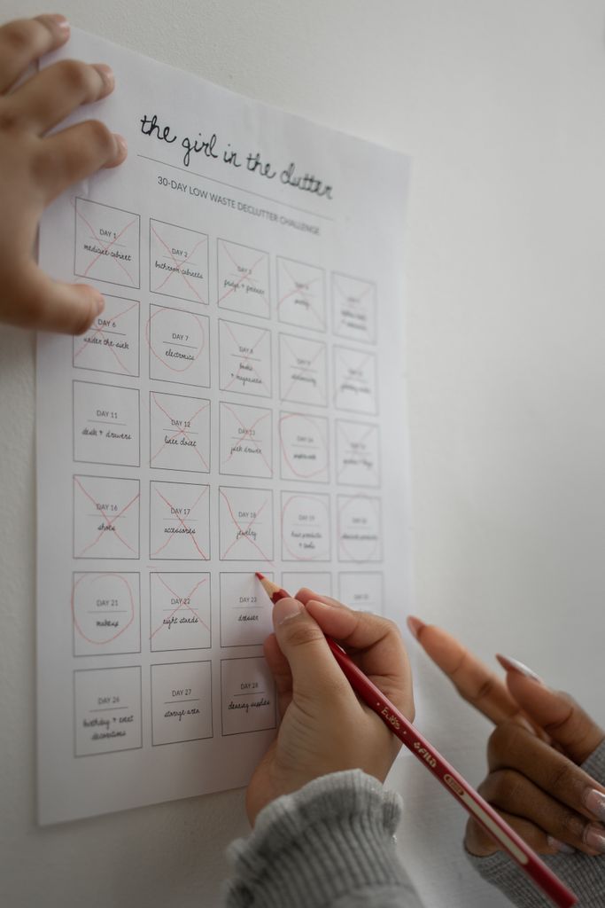 Crop unrecognizable female with manicure and child crossing out list on paper on white background