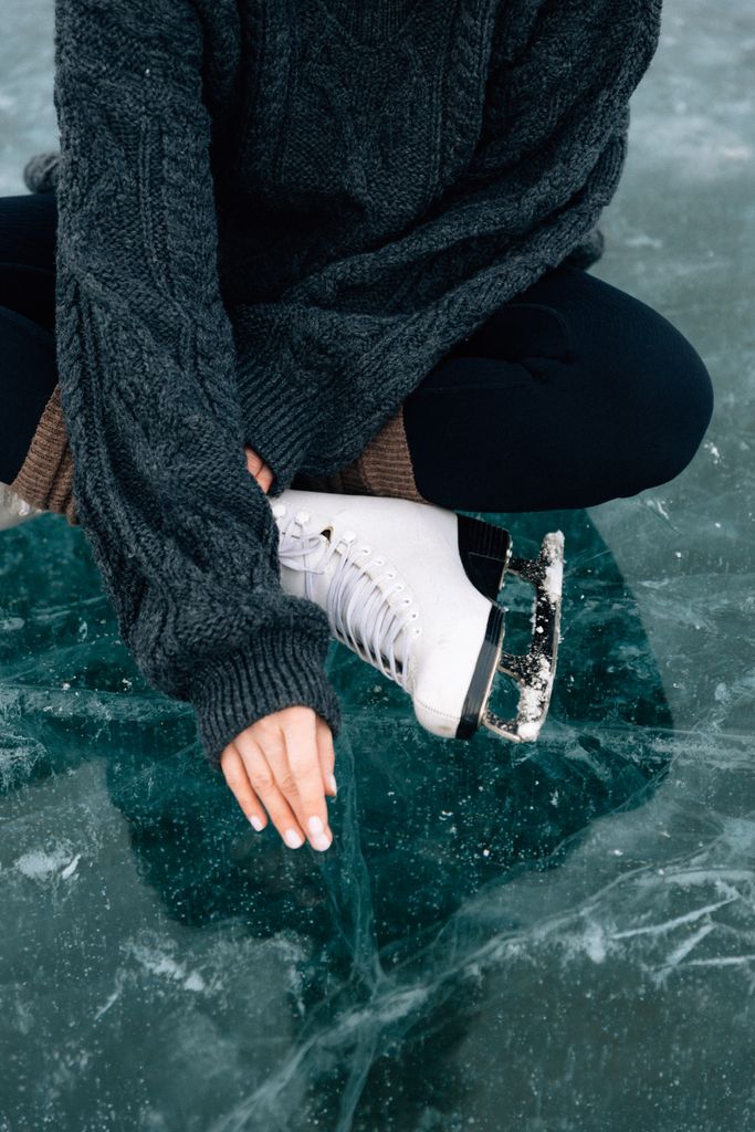 Cropped image of a person sitting on ice, wearing a sweater and ice skates in a winter setting.