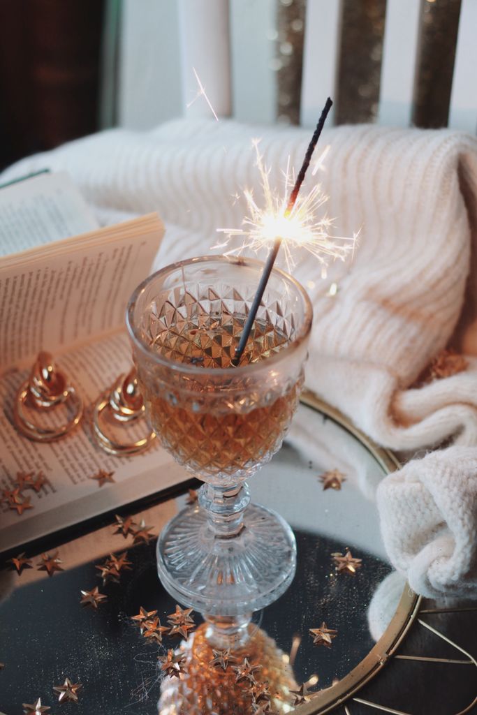 Elegant glass with drink and sparkler on a reflective surface, creating a festive vibe nye at home