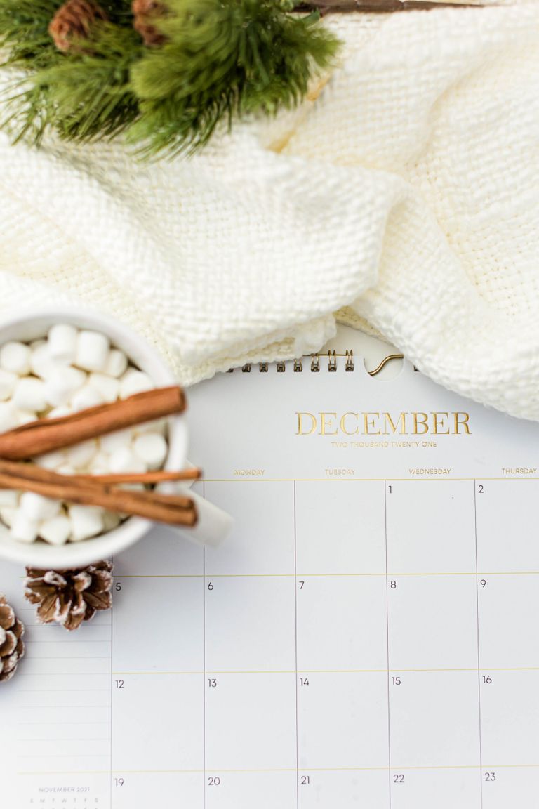 Flat lay of a December calendar with hot chocolate, pine branches, and cinnamon sticks, creating a cozy winter vibe.