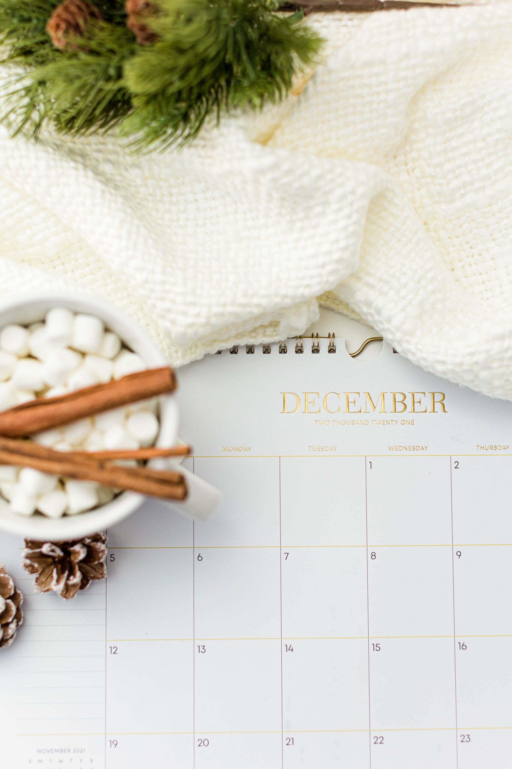 Flat lay of a December calendar with hot chocolate, pine branches, and cinnamon sticks, creating a cozy winter vibe.