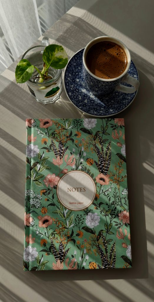 Floral notebook with a cup of coffee and plant creating a cozy workspace vibe.