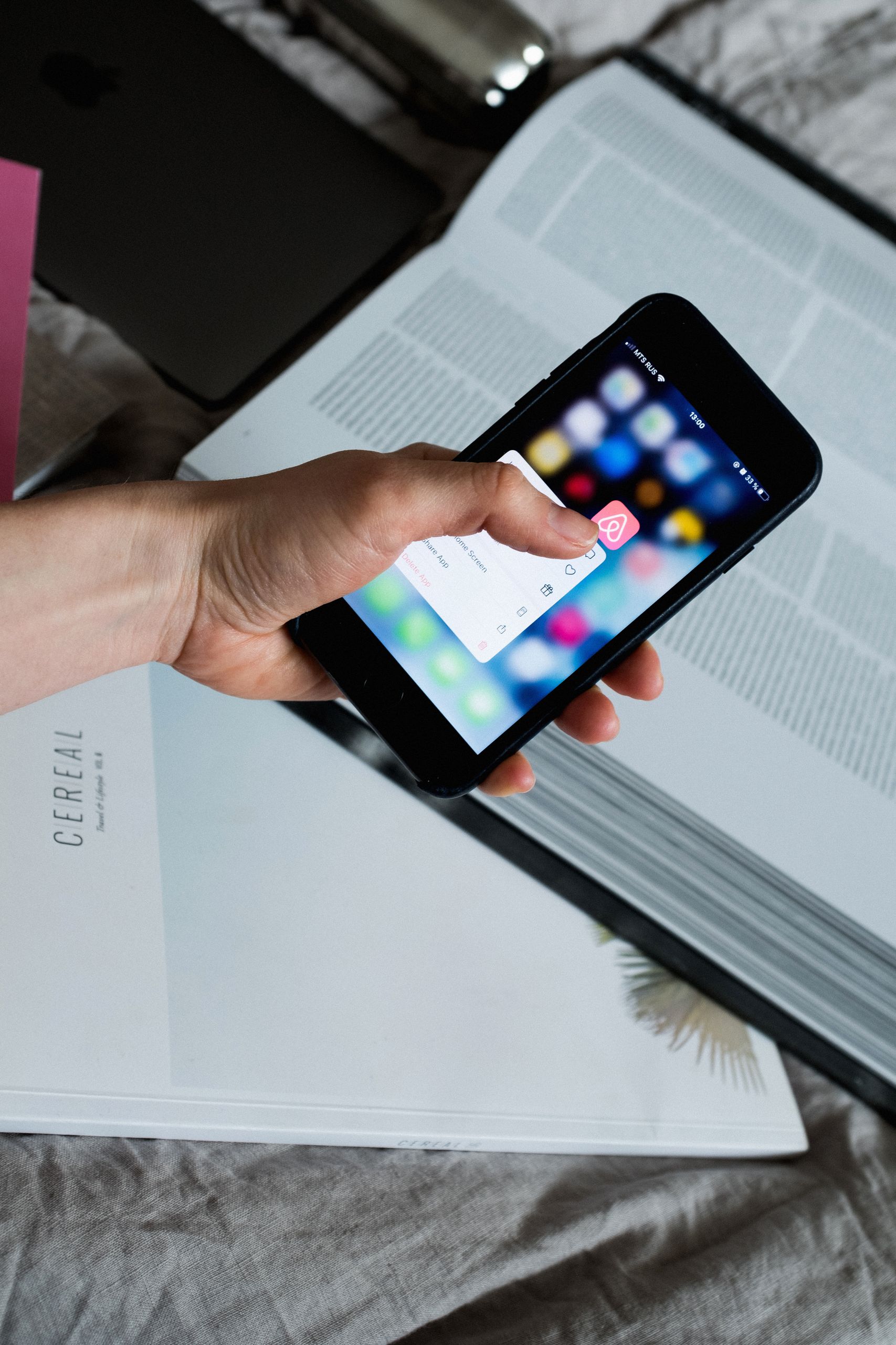 From above of crop anonymous person taking cellphone and touching screen with pop up window while having gadget above open textbook on bed sheet