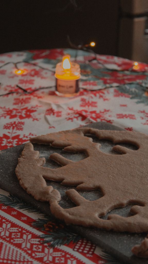 Gingerbread dough shaped like a tree on festive-themed table beside lit candle, perfect for holiday baking.