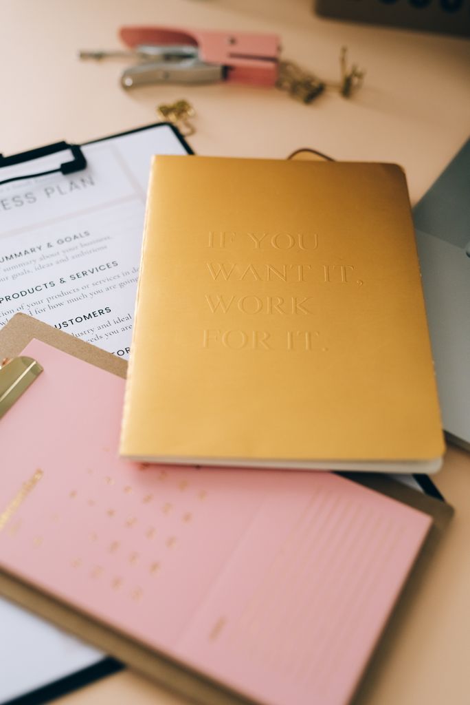 Golden and pink notebooks on a desk symbolize motivation and planning.