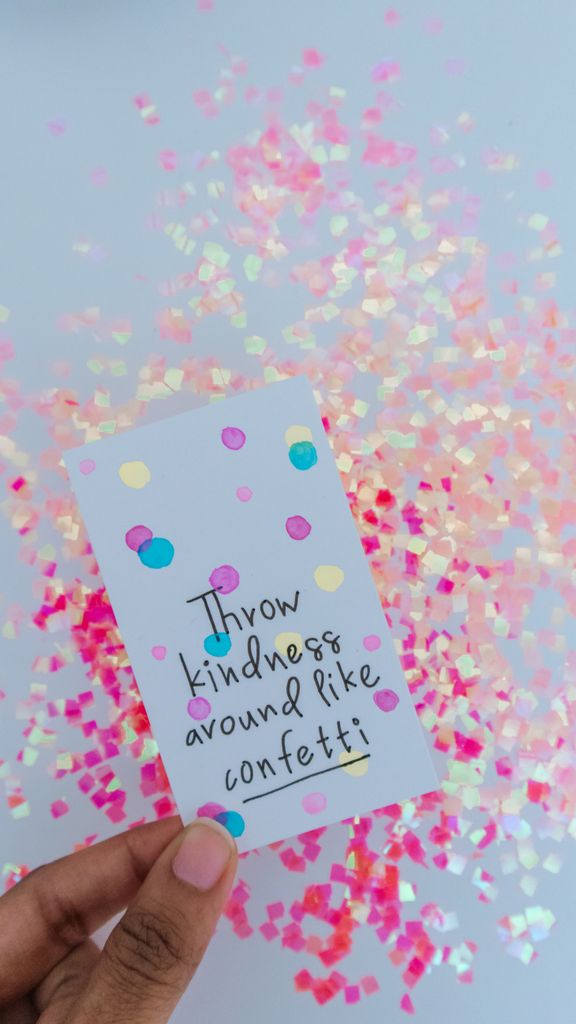 Hand holding a card with 'Throw kindness around like confetti' message against colorful confetti background.February Affirmations