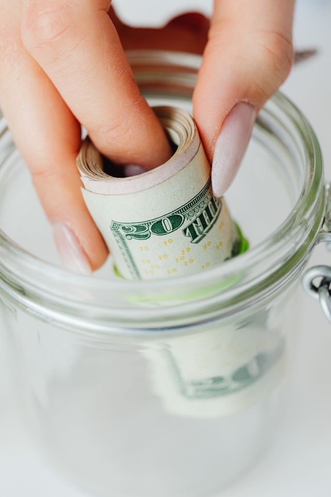 Hand placing rolled US dollars into a glass jar, representing Christmas savings challenge