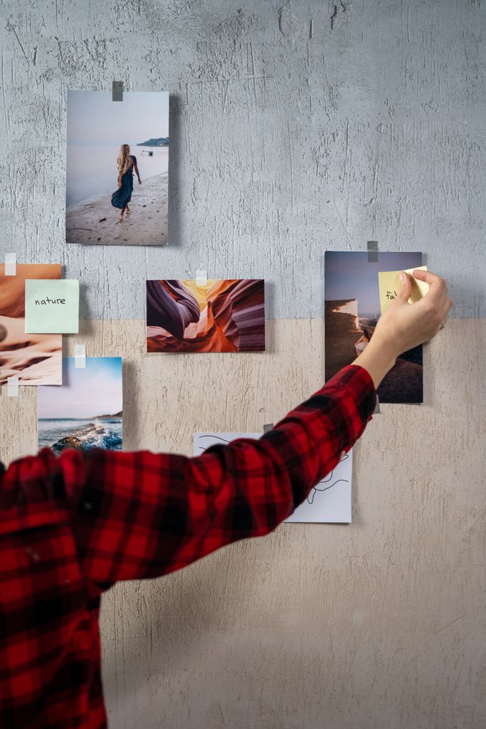 Hand placing sticky notes on a moodboard with travel and nature photos.