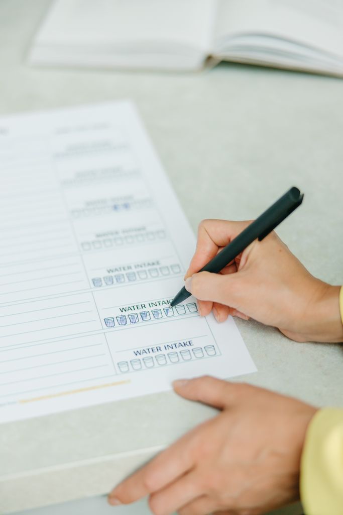 Hands filling out a nutrition plan with a focus on water intake. Ideal for health and wellness themes.
