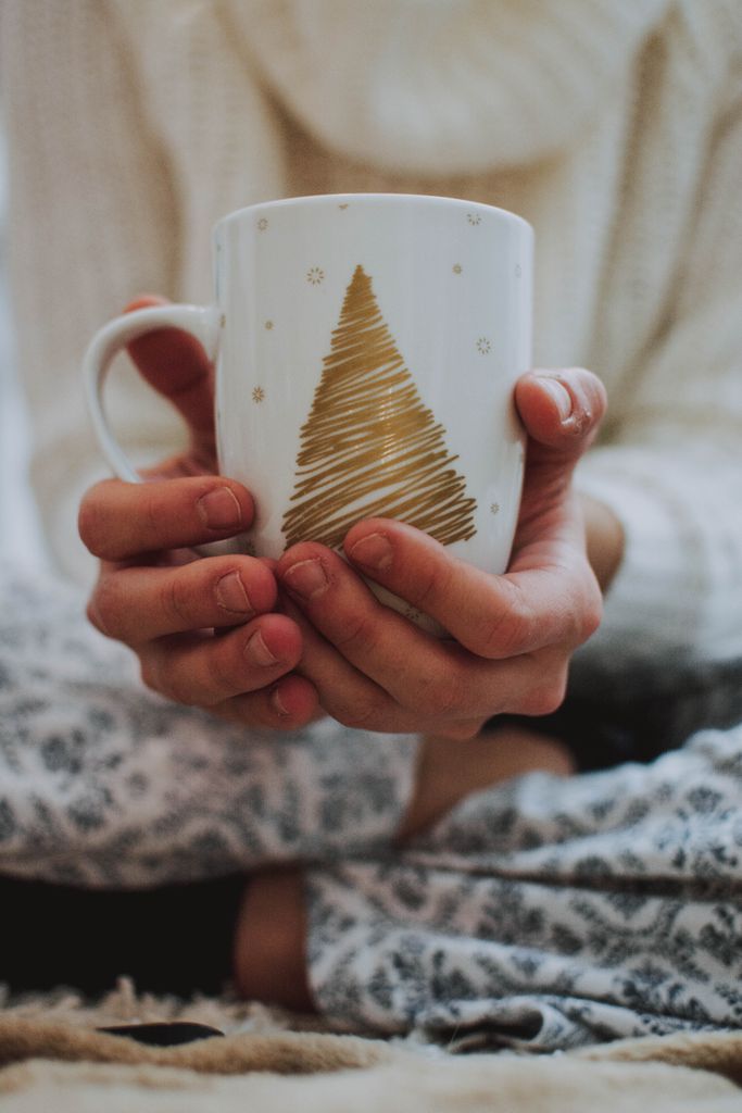 Hands holding a festive mug with a Christmas tree design, perfect for cozy winter moments.