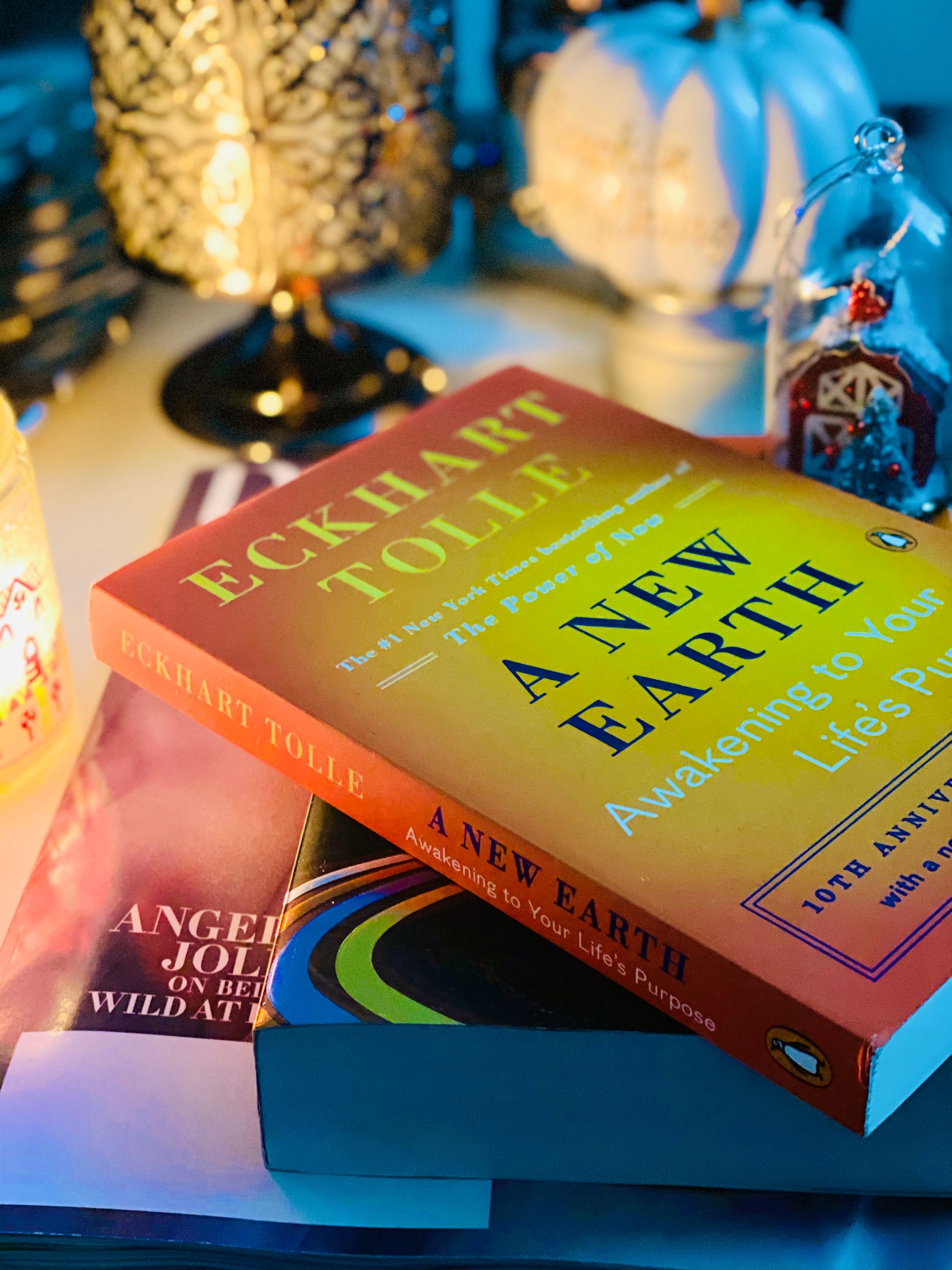 High angle composition of stacked books in softcover placed on bedside table near decorative souvenirs and candleholders with burning tealight in evening