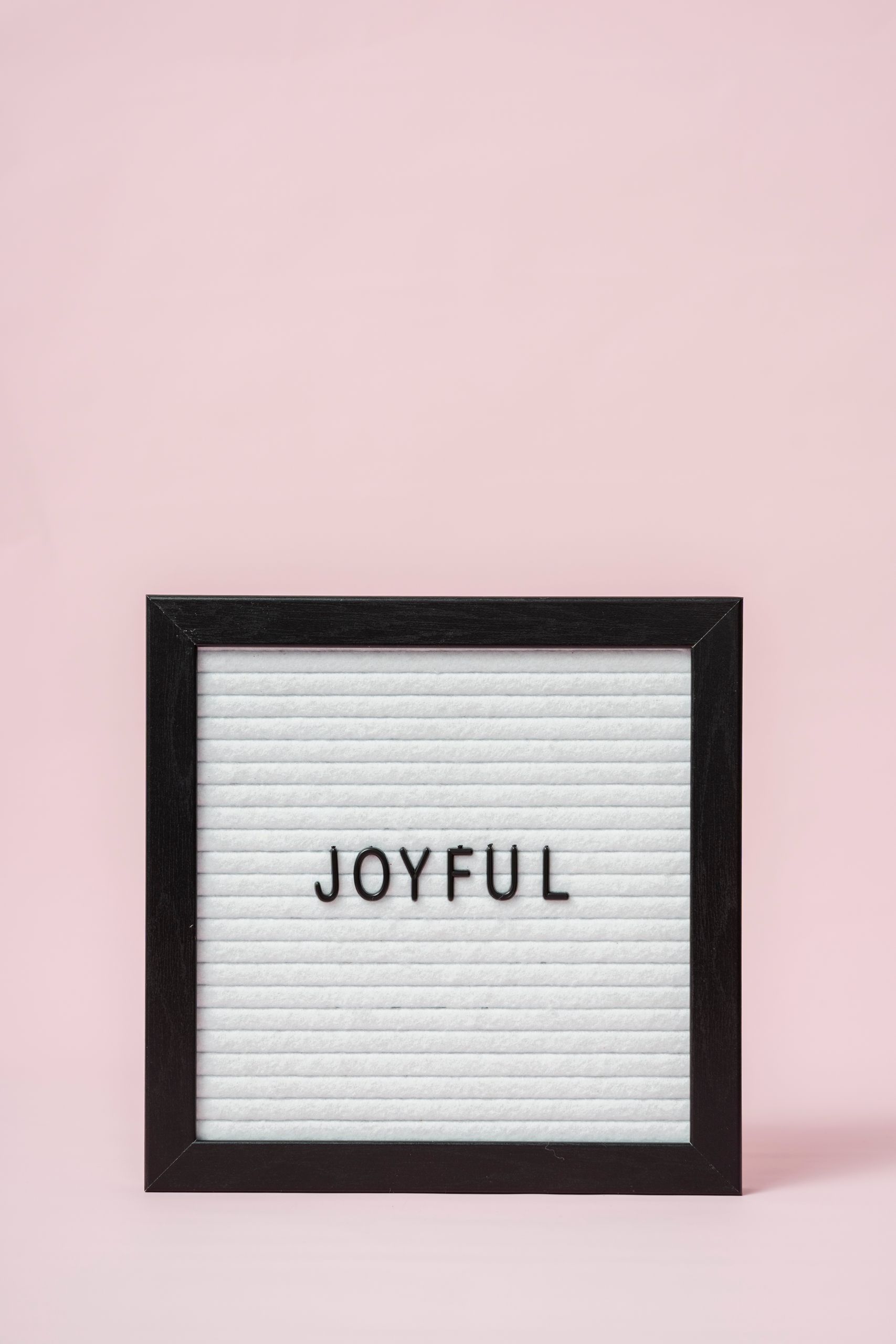Letter board with 'Joyful' text on a minimalist pink background, perfect for positive messages.