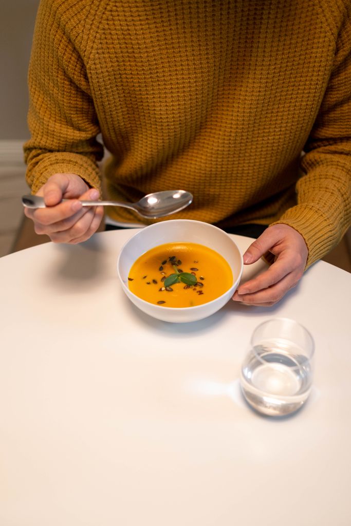 Man enjoying a bowl of pumpkin soup indoors, showcasing a cozy lifestyle setting.